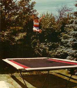 A young 10-year-old gymnast bounces 10 feet high in a sitting position above her Backyard Pro® gymnastics training trampoline.showing perfect form & control. Her Backyard Pro® trampoline is above ground on her lawn outside with trees and bushes in the background. In addition to fun and recreation, every Backyard Pro® trampoline is an ideal sports training platform especially for gymnastics and other aerobatic type sports.