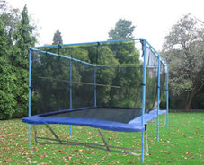 A Backyard Pro® trampoline sits above ground on a green lawn with evergreen trees and bushes in the background. It has blue pads with a black standard outdoor bed. Around the periphery of the trampoline is an attached safety enclosure net which is an optional accessory that we offer.