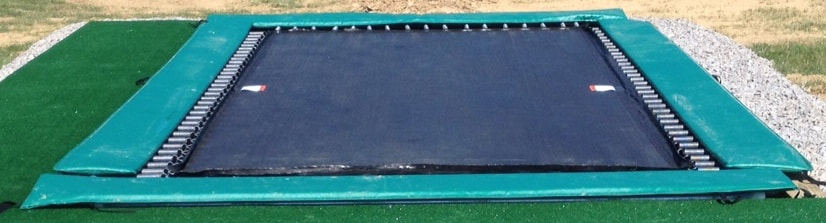 Our standard width green safety pads are shown on a Backyard Pro® ground-level trampoline with a black standard outdoor bed and plated springs. Our standard pads fully cover the frame and most of the extended spring but leave about 2 inches of the spring next to the bed exposed for better performance especially at ground level. The trampoline has Astroturf along one end and one side and there is white limestone gravel along the other end and side.